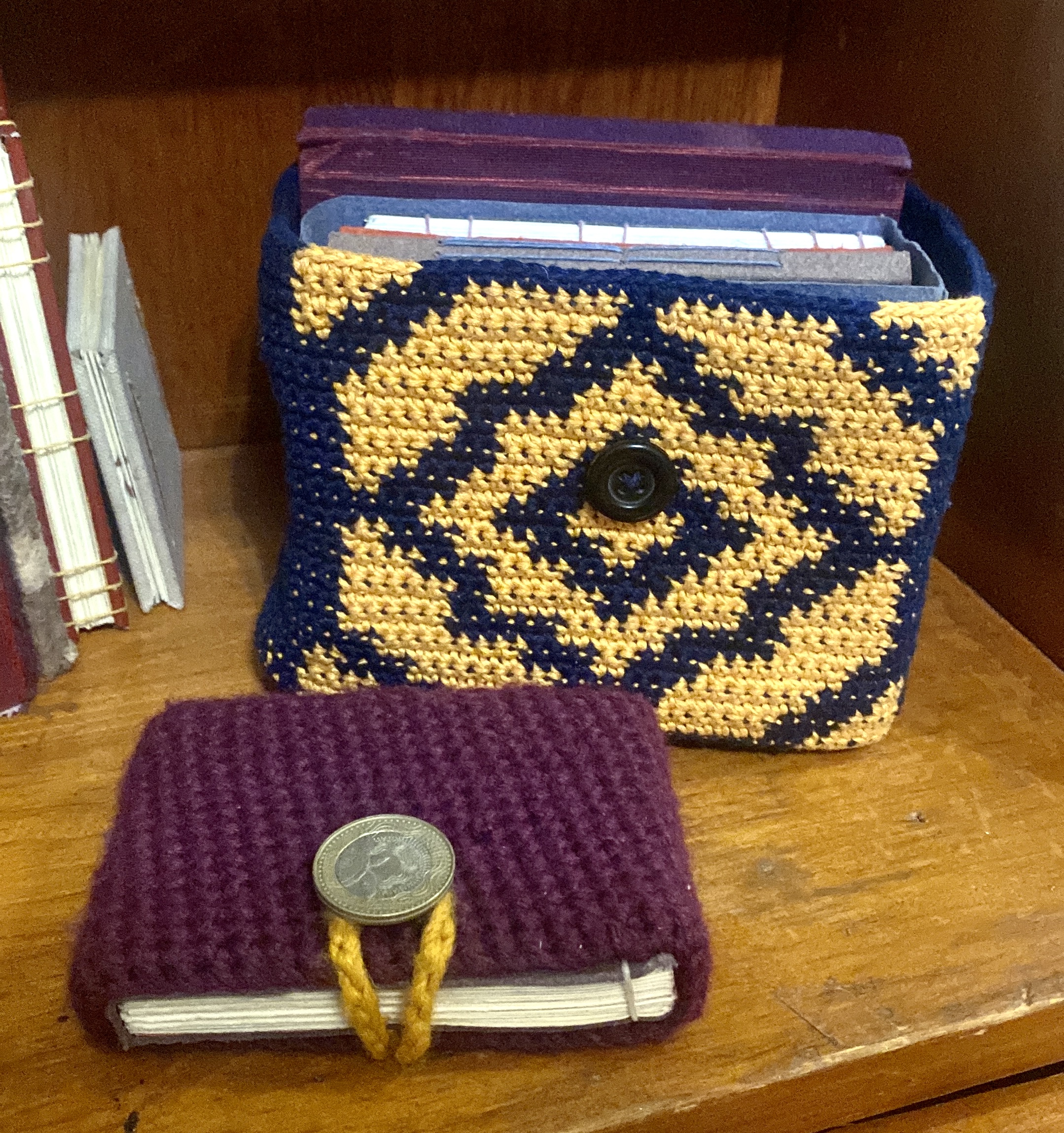 A crochet box with books inside behind a small book with a crochet cover